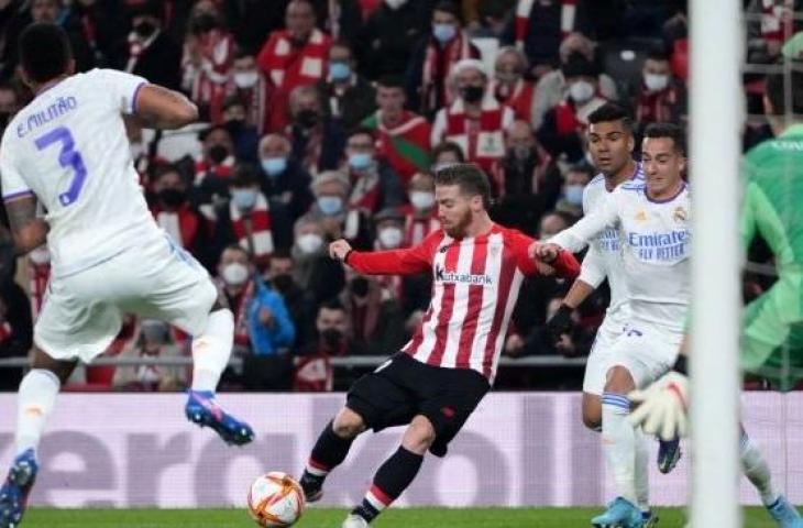 Penyerang Athletic Bilbao, Iker Muniain (tengah) menembak bola melewati gelandang Real Madrid Casemiro dan Lucas Vazquez selama pertandingan perempat final Copa del Rey di Stadion San Mames, Jumat (4/2/2022) dini hari WIB. (CESAR MANSO / AFP)