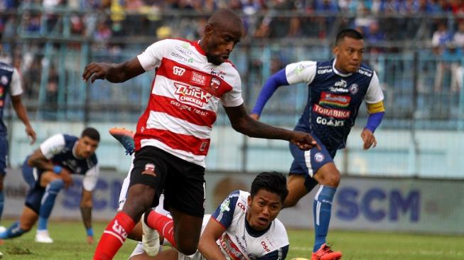 Pesepak bola Madura United, Greg Nwokolo (kiri) lolos dari hadangan panjaga gawang Arema FC, Utam Rusdiana (bawah) dalam pertandingan Liga I di Stadion Kanjuruhan, Malang, Jawa Timur, Senin (17/9). Arema mengalahkan Madura United dengan skor akhir 2-0. ANTARA FOTO/Ari Bowo Sucipto