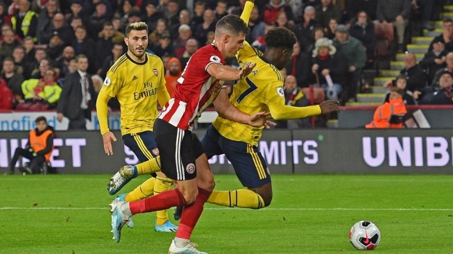 Striker Arsenal, Bukayo Saka (paling kanan) dilanggar bek Sheffield United (tengah), John Egan pada lanjutan Liga Primer Inggris 2019/20 di Stadion Bramall Lane, Selasa (22/10/2019). [OLI SCARFF / AFP]