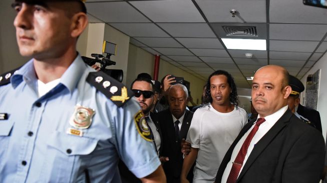 Mantan pemain timnas Brasil, Ronaldinho dikawal oleh polisi meninggalkan kantor pengadilan di Asuncion, ibu kota Paraguay, Sabtu (7/3). [Foto AFP]