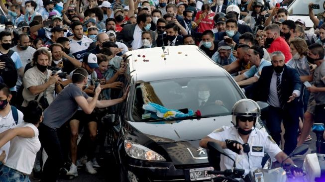 Foto yang dirilis Telam menunjukkan para penggemar berkerumun di samping mobil jenazah yang membawa mendiang legenda sepak bola Argentina Diego Armando Maradona dalam perjalanan dari istana kepresidenan Casa Rosada ke pemakaman  Jardin Bella Vista, di Buenos Aires pada Kamis (26/11/2020) waktu setempat. [Raul FERRARI / TELAM / AFP]