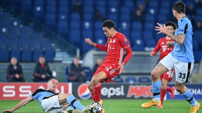 Gelandang Bayern Munich, Jamal Musiala mendapatkan tekel dari gelandang Lazio Adam Marusic (kiri) dalam laga leg pertama babak 16 besar Liga Champions antara Lazio vs Bayern di Stadion Olimpico, Roma, Rabu (24/2/2021) dini hari WIB. [Alberto PIZZOLI / AFP].